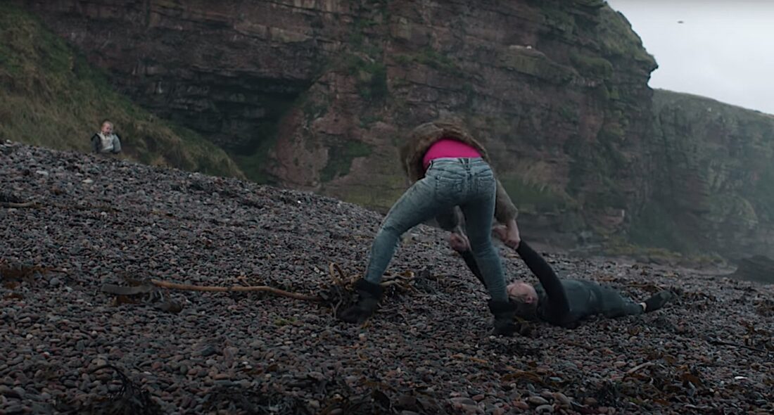 Scarlett Johansson's alien drags a victim down a rocky beach, past a crying baby, in Jonathan Glazer's Under the Skin